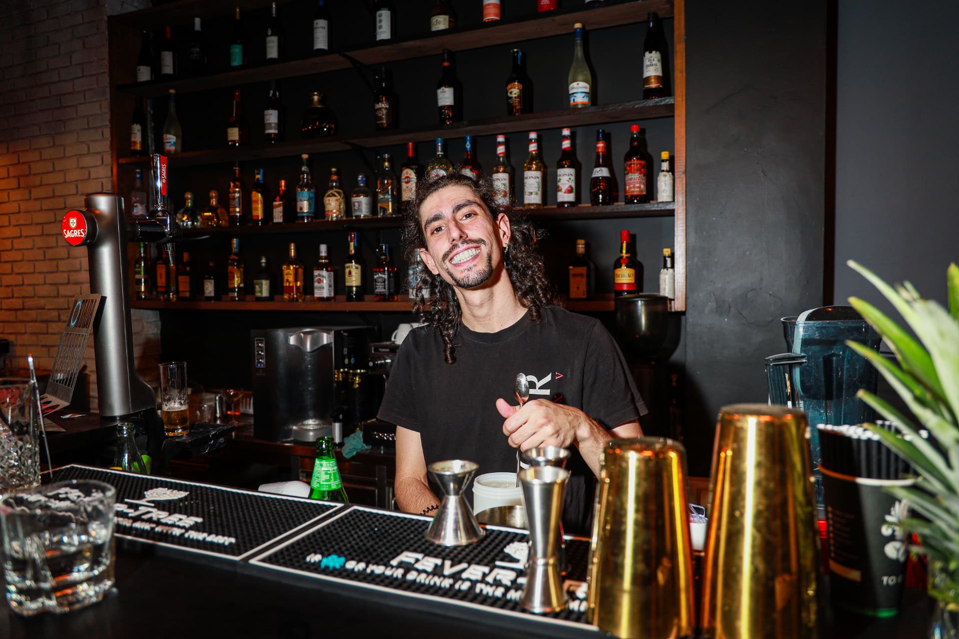 Bartender smiling behind the bar at Enora, with bottles and cocktail tools in front of him